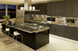 Diseño de cocina con aire industrial, muebles de cocina en color oscuro, campana y encimera de acero y electrodomésticos a la vista